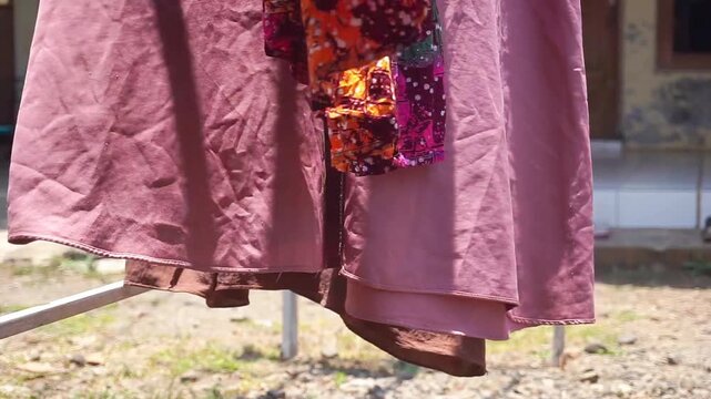 Colorful traditional batik clothing hanging and drying outdoors on a clothesline under bright sunlight during a warm day.
