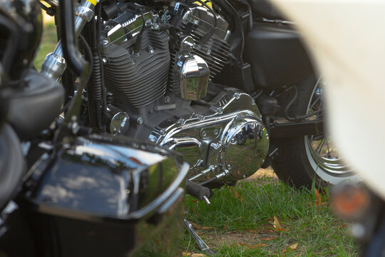 Close-up view of motorcycle engine and chrome transmission casing with grass and part of rear wheel visible in foreground.