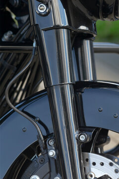 Close-up of front fork and brake assembly on black motorcycle showing glossy suspension tubes, brake caliper, brake line, and ventilated brake disc.