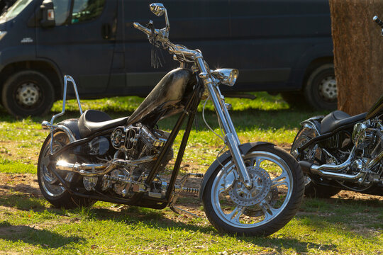 Custom black chopper motorcycle parked on grassy ground with chrome engine and extended front fork visible in side view.