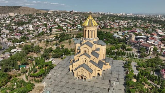 Aerial drone view of the Holy Trinity Cathedral of Tbilisi, also known as Sameba, featuring its golden dome, monumental architecture and panoramic cityscape in Georgia.