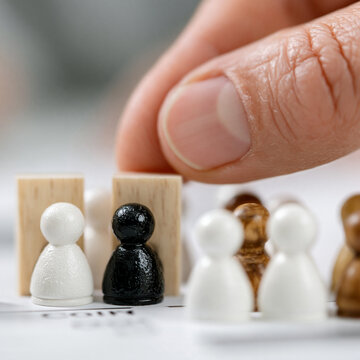 Hand selecting a black wooden pawn from a set of white pieces on a game board with piece