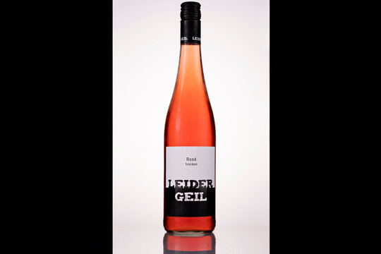Front view of a Leider Geil dry ros&eacute; wine bottle with a black screw cap and black-and-white label. Backlighting reveals the wine&rsquo;s salmon-pink and coral tones against a white background framed by blac