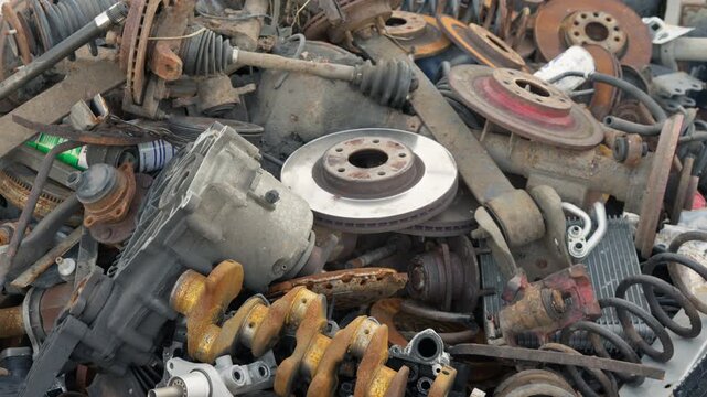 Discarded car scrap metal falls onto a massive recycling pile at an industrial salvage yard. Rusted iron waste undergoes sorting for raw material disposal.