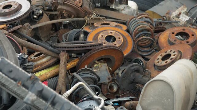 Rusty car scrap metal accumulates in a massive heap at an outdoor salvage yard. Weathered automotive iron and discarded tires undergo collection for metal recycling.