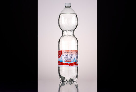 Front view of a Gut & G&uuml;nstig Still 1.5 litre natural mineral water bottle with a white screw cap and red, blue, and white EDEKA-branded German label. Backlit studio photograph on a reflective surface