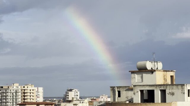 Rainbow Arching Over City Rooftops Against Cloudy Sky After Rain