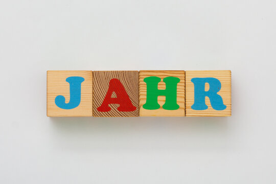 Wooden alphabet blocks in natural wood and bright colors form the German word Jahr , which translates to year in English