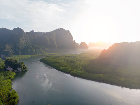 Drone shot of scenic winding river flowing through dense green mangrove forest surrounded by limestone karst mountains during morning sunrise. Nature travel and ecotourism concept.