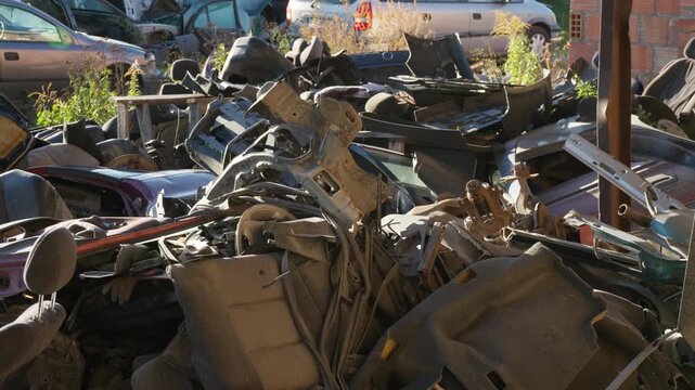 Disassembled car parts and interior trim scrap pile up at an auto salvage yard. Weathered vehicle panels and metal brackets await sorting for recycling disposal.