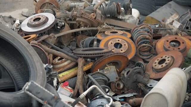 Discarded car scrap metal pile accumulates at an outdoor salvage yard. Weathered automotive iron parts and used tires await collection for metal recycling.