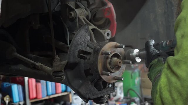 Auto mechanic removes rust from wheel hub flange using a rotary wire brush. Cleaning metal prepares brake rotor mounting during garage workshop maintenance.