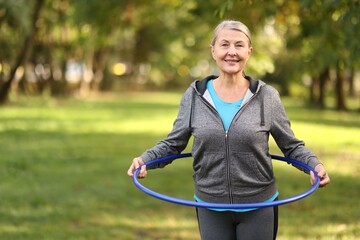 Senior woman exercising with hula hoop outdoors, space for text © New Africa