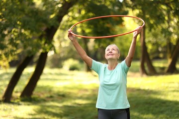 Senior woman exercising with hula hoop outdoors, space for text © New Africa