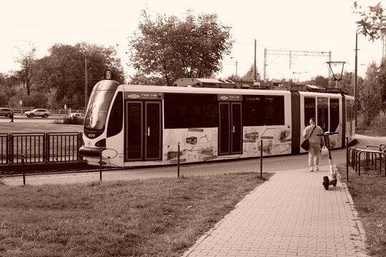 Sepia-toned MPK Poznań tram beside a pedestrian path on a leafy street in Poland