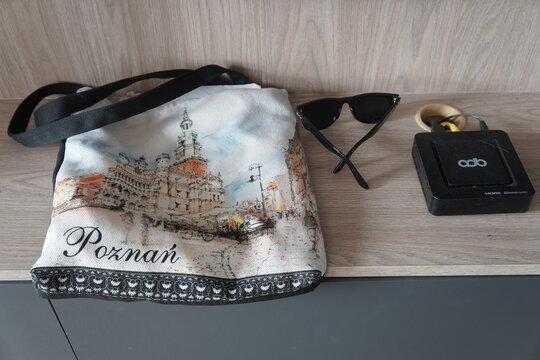Souvenir tote bag printed with Poznań architecture beside sunglasses and a media device