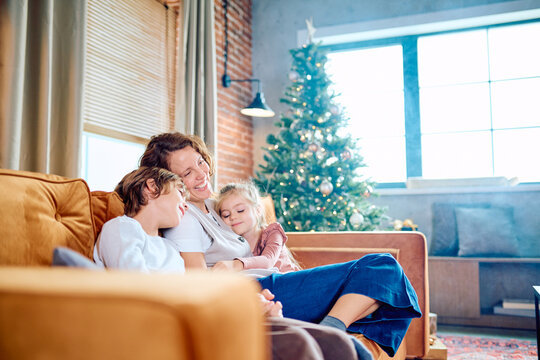 Happy family spending holiday time at home. Mother embracing children on a cozy sofa with a decorated Christmas tree