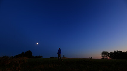 Silhouette of a person in nature observing night sky, Moon, stars and planets from a remote location. © astrosystem