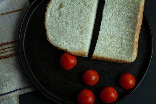 bread slices in a black plate with whole cherry tomatoes,  on black background with a table cloth on side