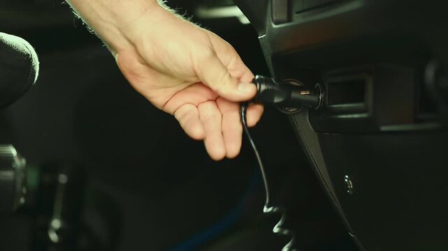 Driver hand inserting charger plug into car cigarette lighter socket slow motion