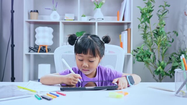 Asian girl drawing on digital tablet with stylus pen at desk in living room for online learning