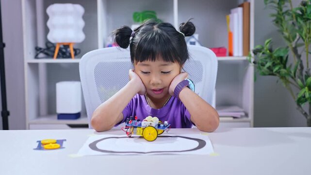 Asian girl watching autonomous line tracking robot car moving on paper track during stem education robotics lesson at desk
