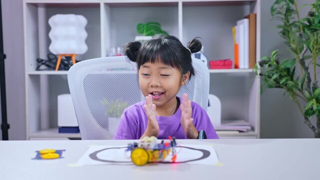 Asian girl student clapping hands with excitement watching autonomous robot follow track in stem classroom