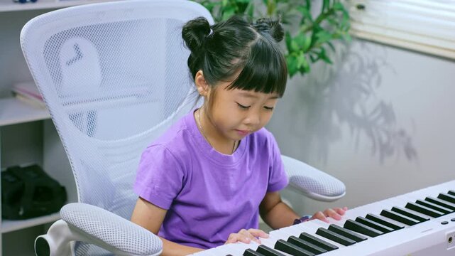 Asian girl practicing piano keyboard at home while smiling and learning musical instrument