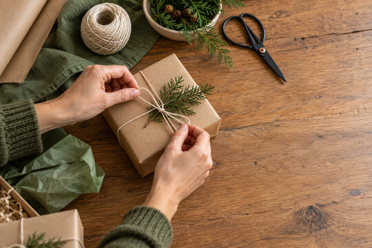Hands wrapping a holiday parcel in kraft paper with string on a wooden table