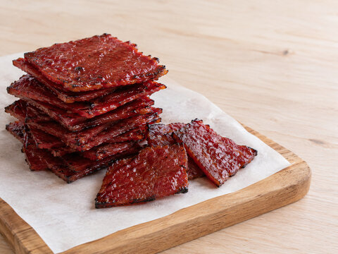Stack of glossy red bak kwa barbecued pork jerky on baking paper (AI generated)