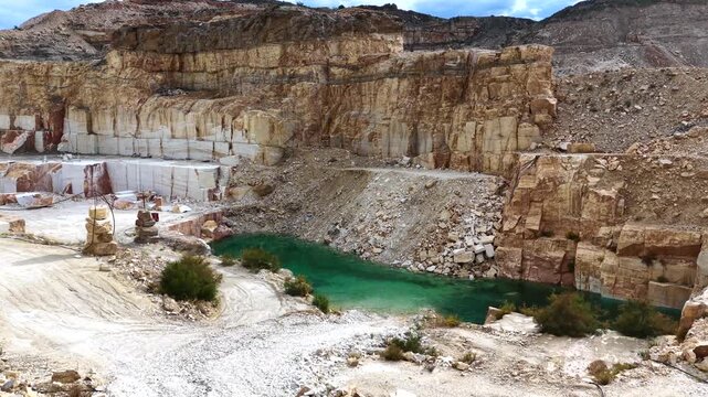 4K b-roll shot of white marble quarry pit with emerald water pond and carved stone walls
