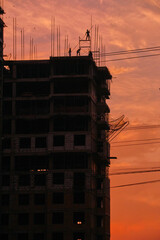 Silhouettes of construction workers building high rise skyscraper against orange sunset sky © Marat
