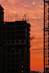 Silhouettes of construction workers building high rise skyscraper against orange sunset sky © Marat