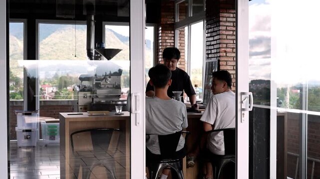 shot from outside looking through glass sliding doors at a barista interacting with customers inside a scenic roastery cafe