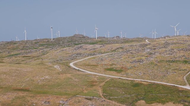 Aerial forward flyover across row of wind turbines on mountain crest in Portugal
