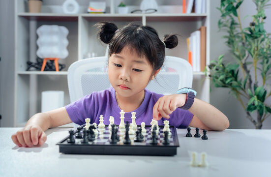 Asian girl playing chess board game thoughtfully indoors, smart kid developing critical thinking strategy and early education skill