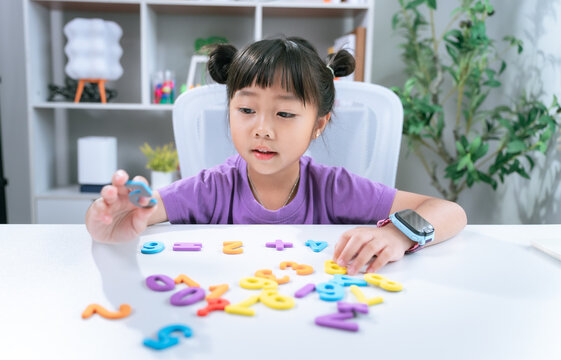Little asian girl solving math equations using colorful numbers on desk during home schooling education