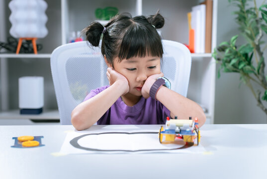 Asian girl testing robotic toy vehicle following line track on classroom desk in stem education concept