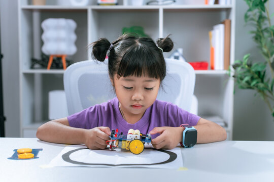 Asian girl testing robotic toy vehicle following line track on classroom desk in stem education concept