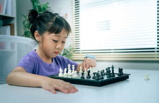 Asian girl playing chess board game thoughtfully indoors, smart kid developing critical thinking strategy and early education skill