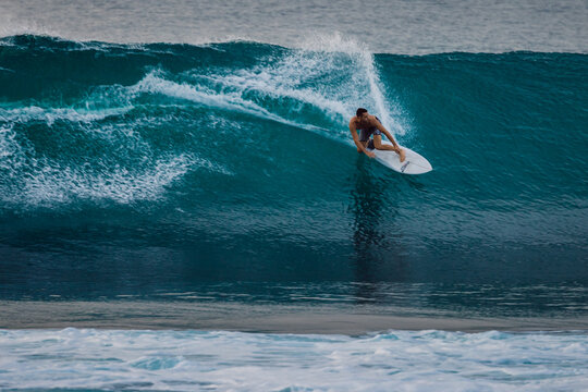 Surfer man riding on surfboard while and carving through a blue wave with water spray