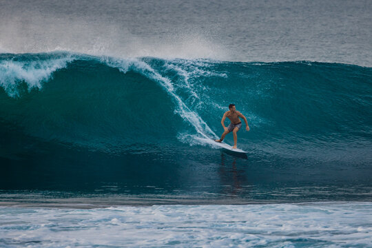 Surfer man riding on surfboard while and carving through a blue wave with water spray