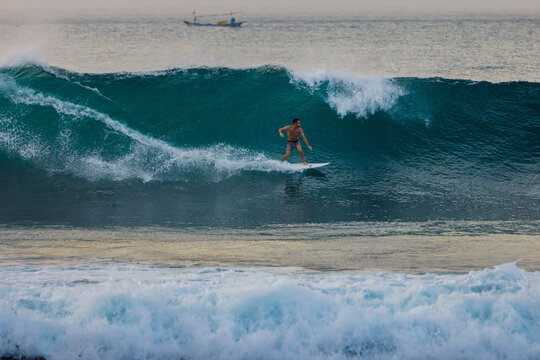 Surfer man crouching low on a white surfboard while carving through a deep blue wave with ocean spray
