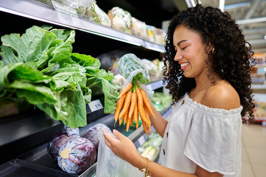 Young woman shopping for fresh organic carrots in supermarket