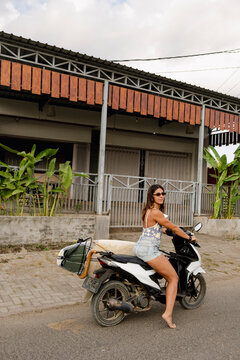 Woman posing on scooter with surfboard in Indonesia