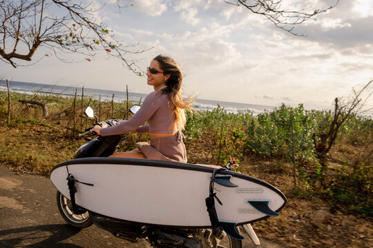 Woman riding scooter with surfboard in Indonesia