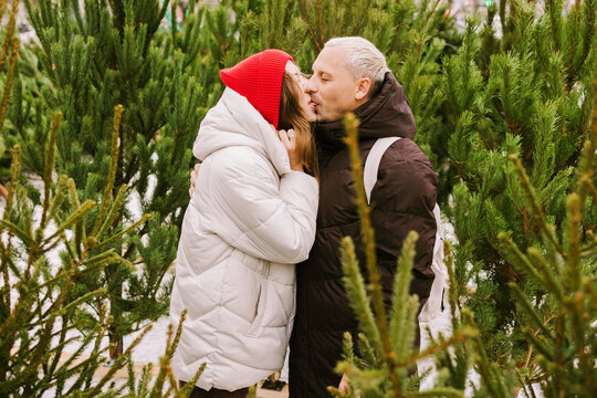 A couple is kissing at a Christmas tree market.