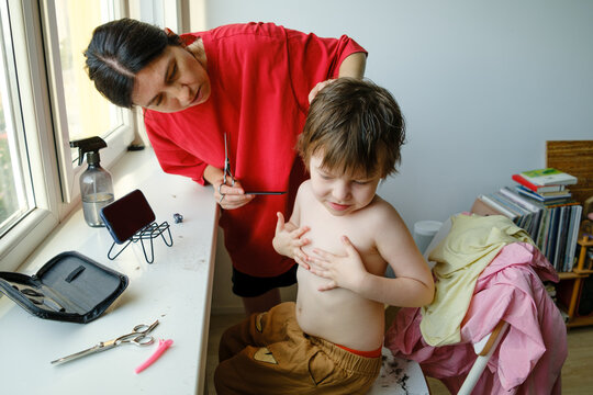 Mother cleaning cut hair off her son after a haircut.