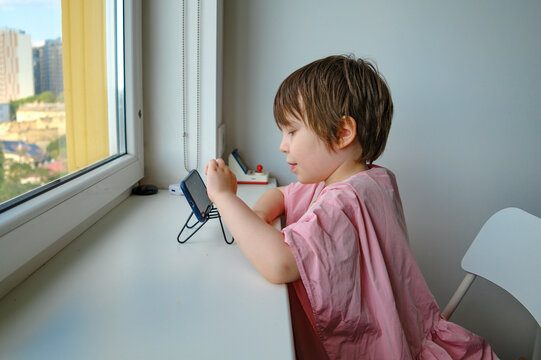 Little boy using smartphone while sitting by the window.