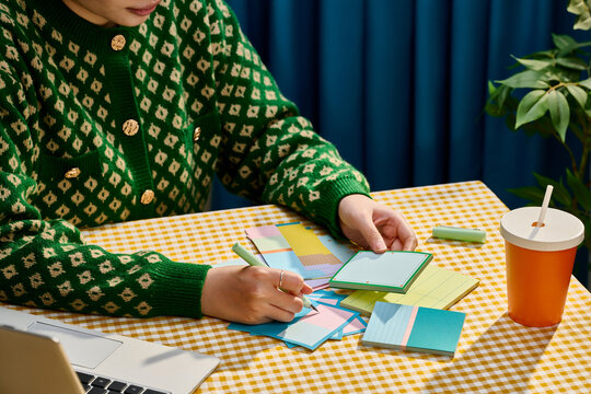 Woman's hands writing on colorful sticky notes at a desk
